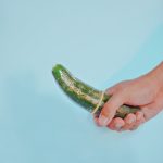 A cucumber wrapped with a condom held in a hand on a blue background, expressing safe sex concept.