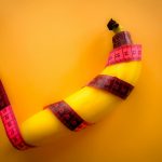 Conceptual image of a banana wrapped with a pink measuring tape on a bright yellow background.