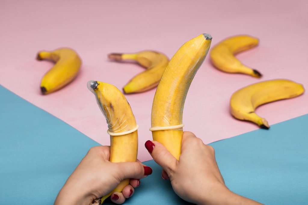 Creative display of bananas with condoms on pastel background, promoting safe sex.