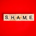Scrabble tiles spelling the word 'Shame' on a vibrant red backdrop.