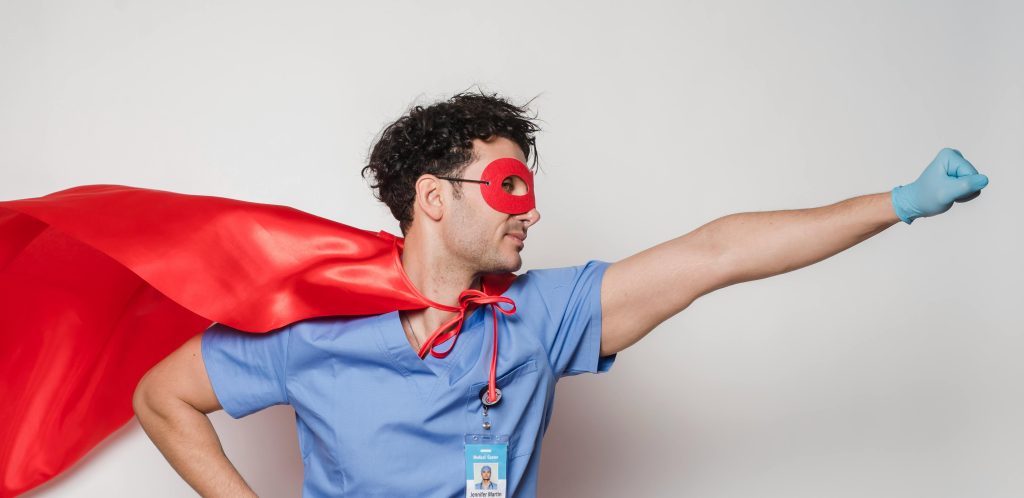 Male healthcare worker wearing a red cape and mask poses as a superhero. Studio shot.