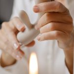 Hands gently holding a rabbit vibrator with a lit candle in the background, depicting intimacy and self-care.